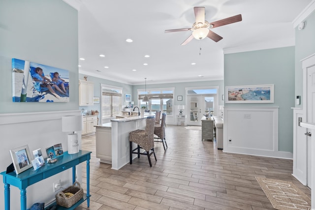 kitchen featuring a breakfast bar, hanging light fixtures, ornamental molding, a kitchen island with sink, and light hardwood / wood-style floors