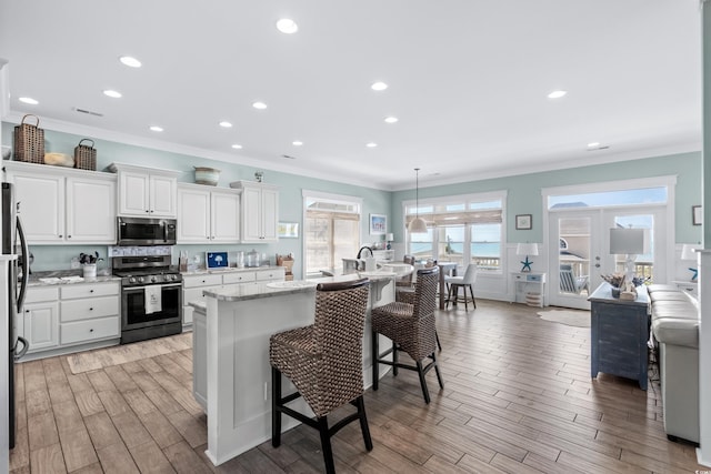 kitchen featuring white cabinets, a kitchen breakfast bar, hanging light fixtures, a kitchen island with sink, and stainless steel appliances