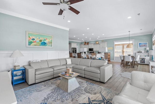 living room with crown molding, ceiling fan, and light wood-type flooring