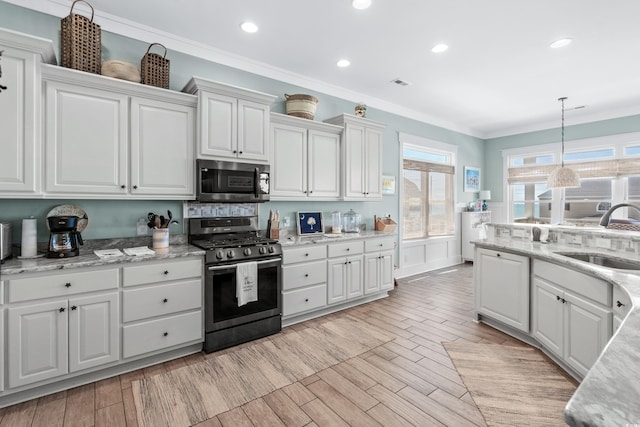 kitchen with appliances with stainless steel finishes, decorative light fixtures, white cabinetry, sink, and ornamental molding