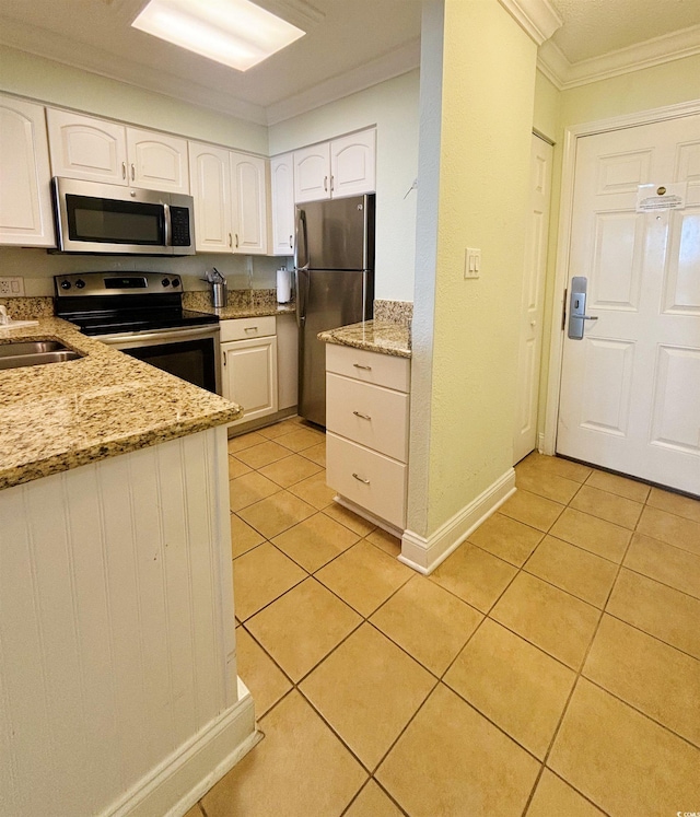 kitchen with appliances with stainless steel finishes, white cabinetry, light stone counters, light tile patterned floors, and ornamental molding