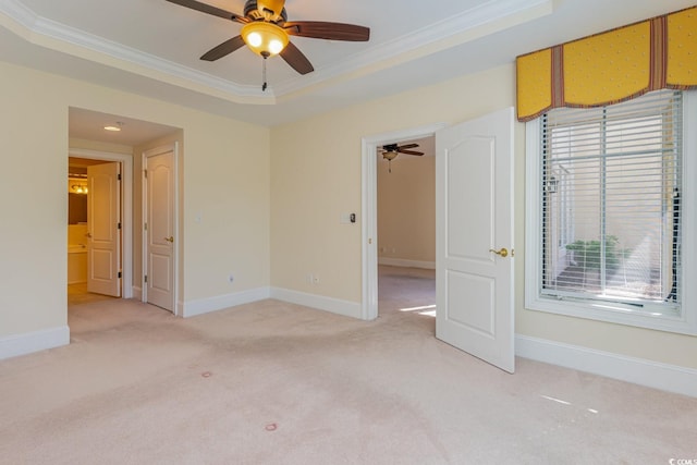 empty room with a tray ceiling, ceiling fan, light colored carpet, and ornamental molding