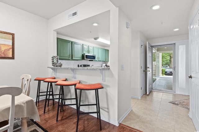 kitchen with green cabinets, light stone counters, kitchen peninsula, a breakfast bar area, and backsplash