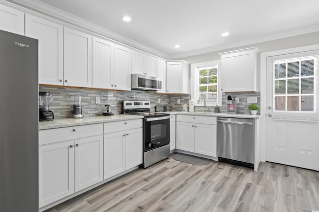 kitchen featuring stainless steel appliances, backsplash, ornamental molding, light wood-type flooring, and white cabinets