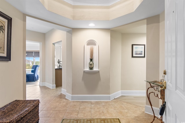 hallway featuring a raised ceiling, crown molding, and light tile patterned flooring