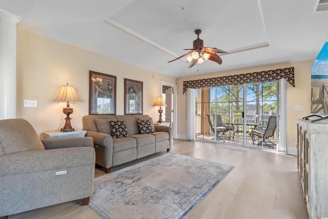 living room with light hardwood / wood-style floors, a raised ceiling, and ceiling fan