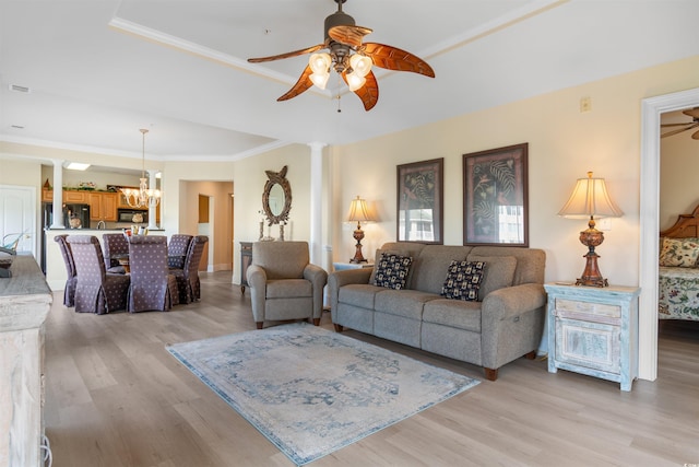 living room featuring ceiling fan with notable chandelier, light wood-type flooring, decorative columns, and ornamental molding