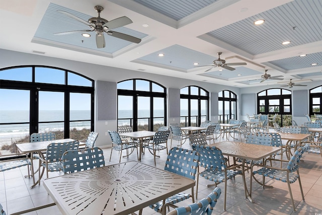 tiled dining room with ceiling fan, a water view, and coffered ceiling