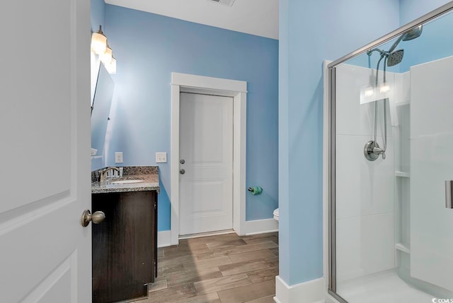 bathroom featuring wood-type flooring, toilet, vanity, and a shower with shower door