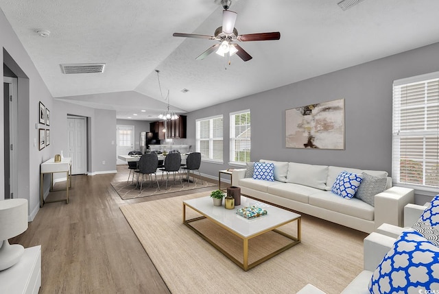 living room featuring ceiling fan with notable chandelier, a textured ceiling, hardwood / wood-style flooring, and vaulted ceiling