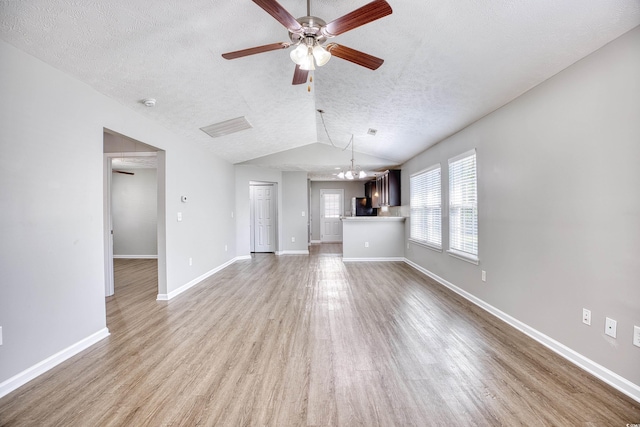 unfurnished living room with light wood-type flooring, ceiling fan with notable chandelier, vaulted ceiling, and a textured ceiling