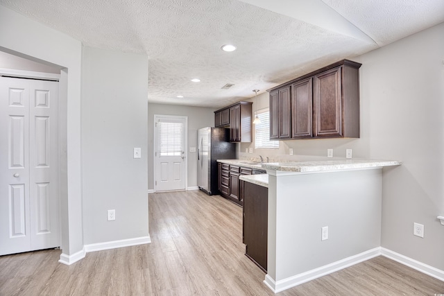 kitchen with dark brown cabinets, light wood-type flooring, stainless steel fridge, and a textured ceiling