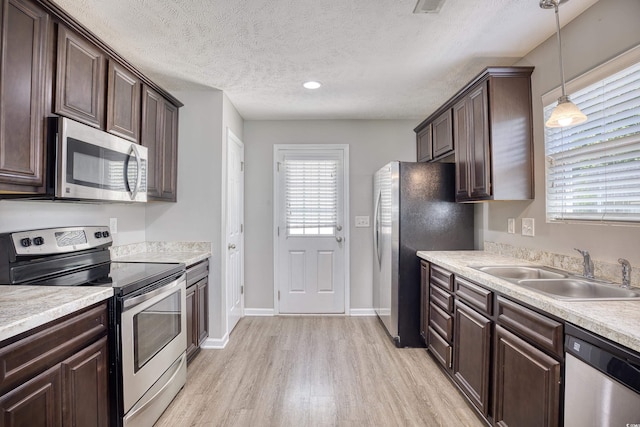 kitchen with dark brown cabinets, stainless steel appliances, light hardwood / wood-style floors, decorative light fixtures, and sink