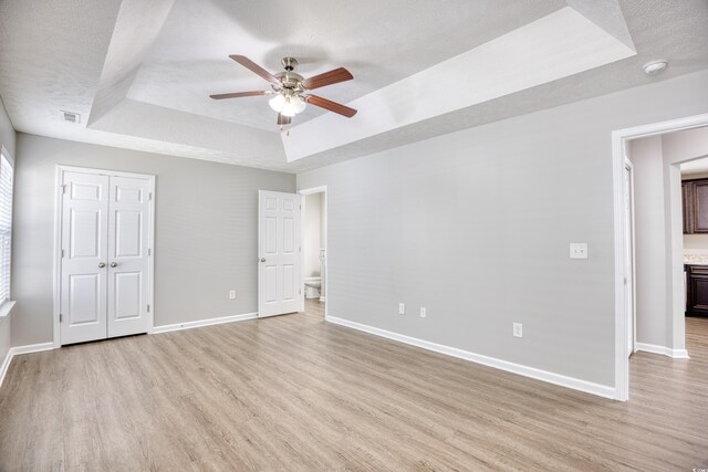 unfurnished bedroom with a closet, ceiling fan, a tray ceiling, light hardwood / wood-style flooring, and ensuite bathroom