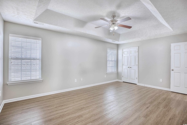 empty room featuring light hardwood / wood-style flooring, a textured ceiling, ceiling fan, and a raised ceiling