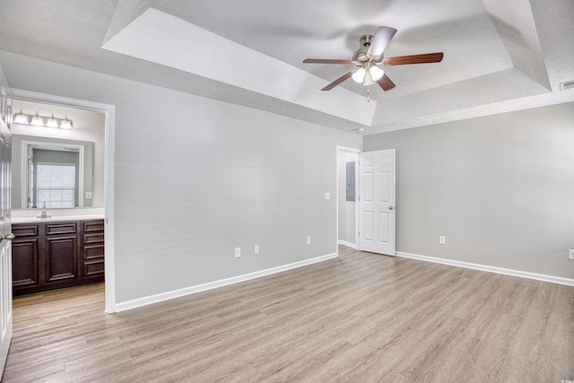 unfurnished bedroom featuring ceiling fan, light wood-type flooring, a raised ceiling, ensuite bathroom, and a textured ceiling