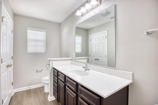 bathroom with a wealth of natural light, vanity, wood-type flooring, and toilet