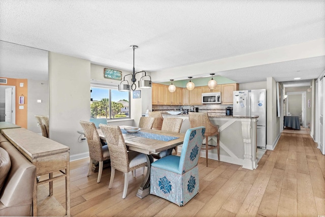 dining area featuring a notable chandelier, light hardwood / wood-style flooring, and a textured ceiling