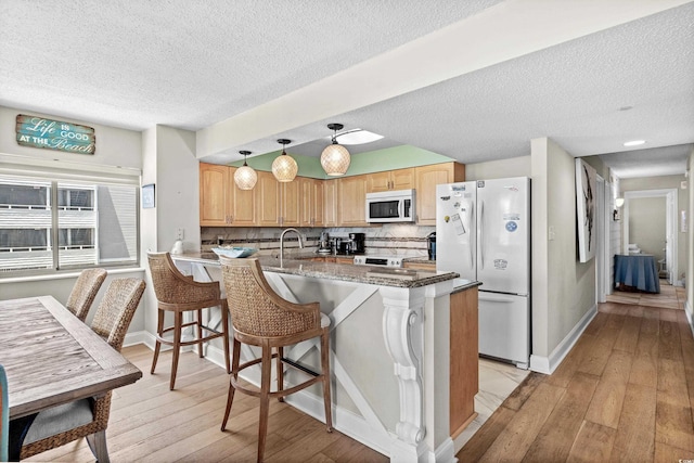 kitchen with decorative light fixtures, light wood-type flooring, dark stone counters, and white refrigerator