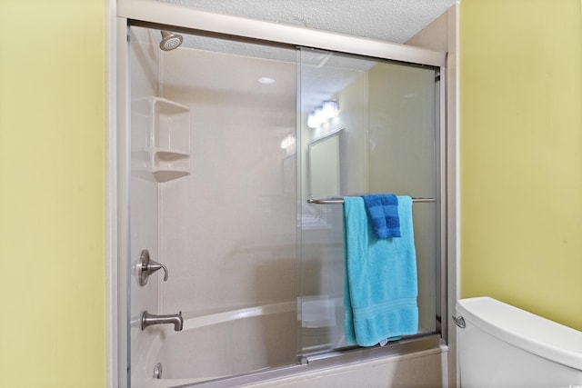 bathroom with combined bath / shower with glass door, a textured ceiling, and toilet