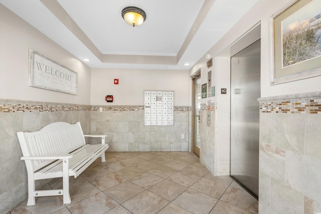 hallway featuring elevator, a raised ceiling, tile walls, and a mail area