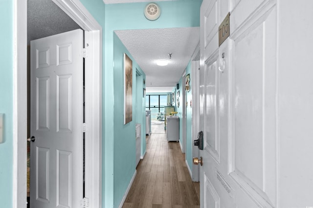 hallway with a textured ceiling and light wood finished floors