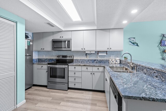 kitchen with sink, dark stone countertops, appliances with stainless steel finishes, light hardwood / wood-style flooring, and kitchen peninsula