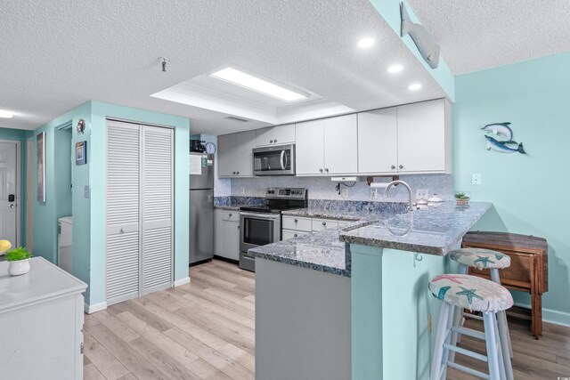 kitchen featuring white cabinets, stone counters, light hardwood / wood-style flooring, and stainless steel appliances