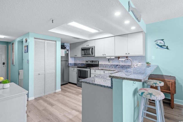 kitchen with a breakfast bar, appliances with stainless steel finishes, dark stone countertops, light wood-type flooring, and a peninsula