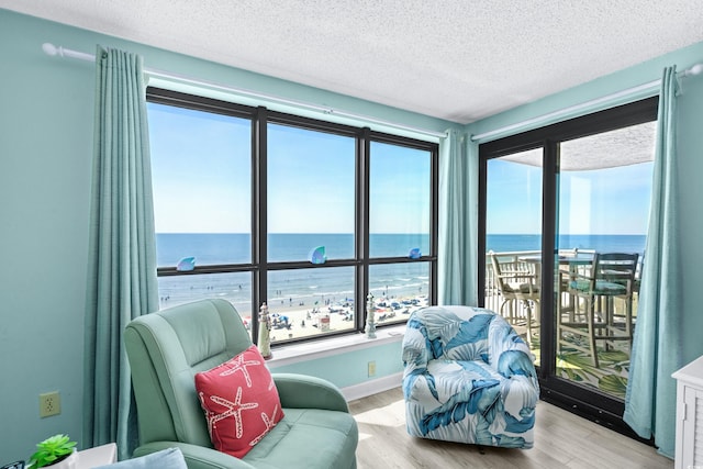 sitting room featuring a textured ceiling, light wood-type flooring, a water view, and baseboards