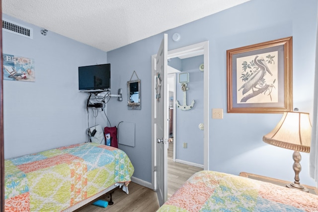 bedroom featuring light wood-style floors, baseboards, visible vents, and a textured ceiling