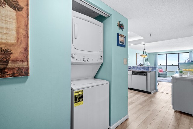 clothes washing area featuring a textured ceiling, light hardwood / wood-style flooring, and stacked washer and clothes dryer