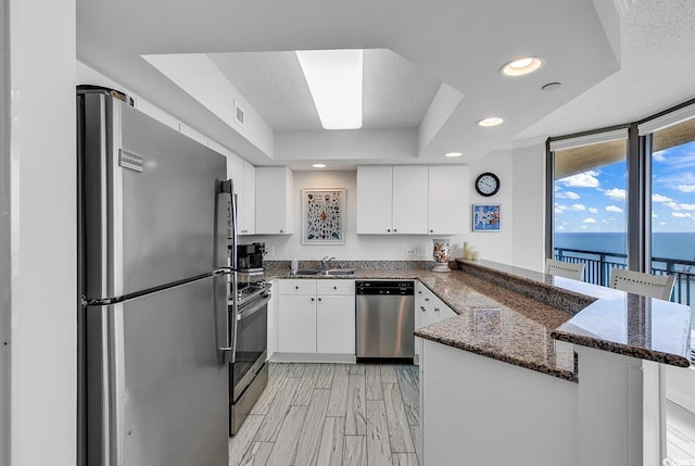 kitchen featuring white cabinets, a water view, kitchen peninsula, and stainless steel appliances