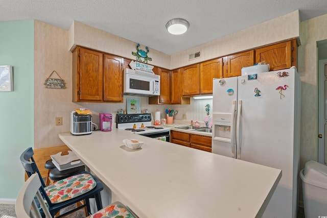 kitchen with a textured ceiling, kitchen peninsula, and white appliances