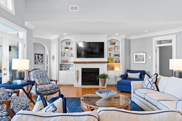 living room with built in shelves, a large fireplace, french doors, ornamental molding, and light hardwood / wood-style flooring