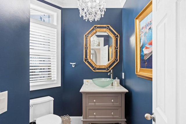 bathroom with an inviting chandelier, crown molding, vanity, and toilet