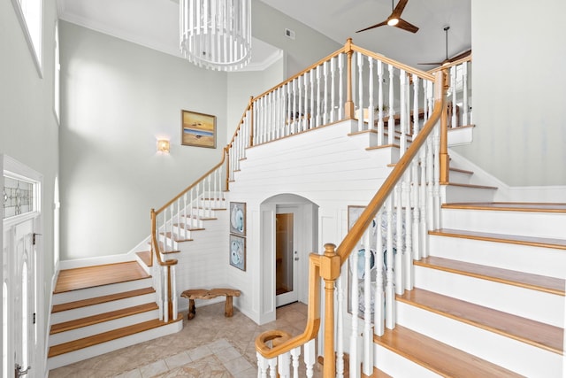 staircase with a towering ceiling, ceiling fan with notable chandelier, light tile patterned floors, and crown molding