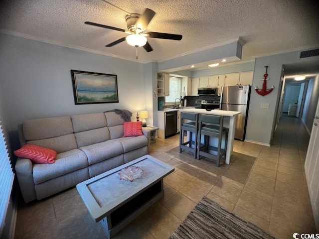 living room with ceiling fan, light tile patterned flooring, ornamental molding, sink, and a textured ceiling