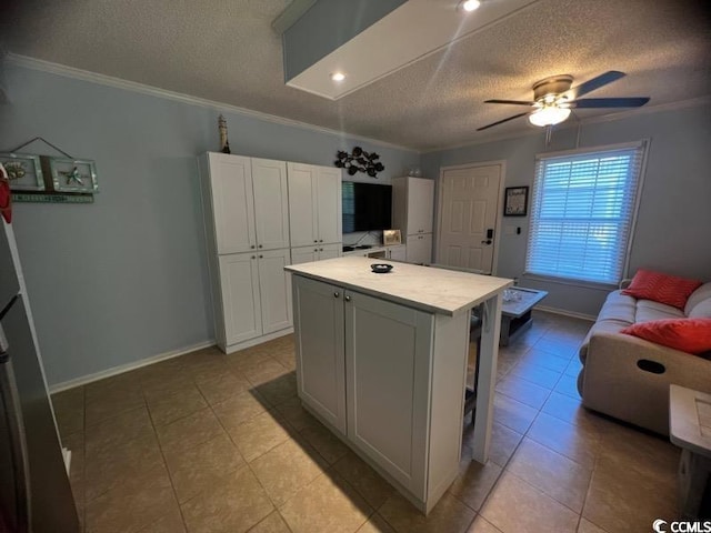 kitchen featuring a textured ceiling, a center island, white cabinetry, ornamental molding, and ceiling fan