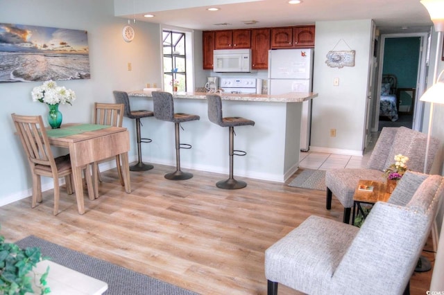 kitchen with light wood-type flooring, a breakfast bar, and white appliances