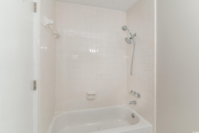 bathroom with a textured ceiling and tiled shower / bath