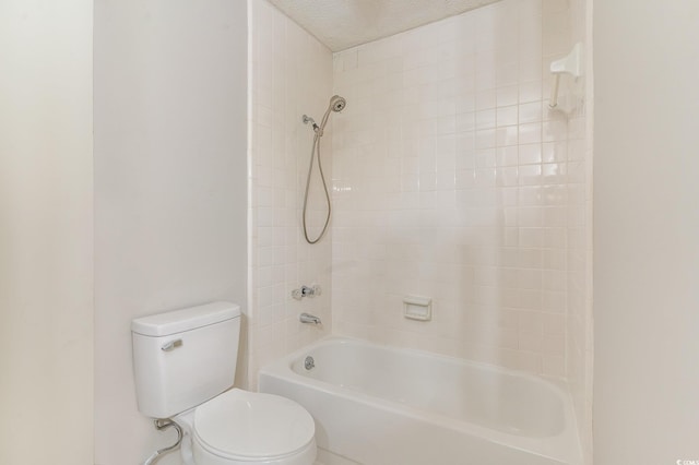 bathroom with a textured ceiling, toilet, and tiled shower / bath combo