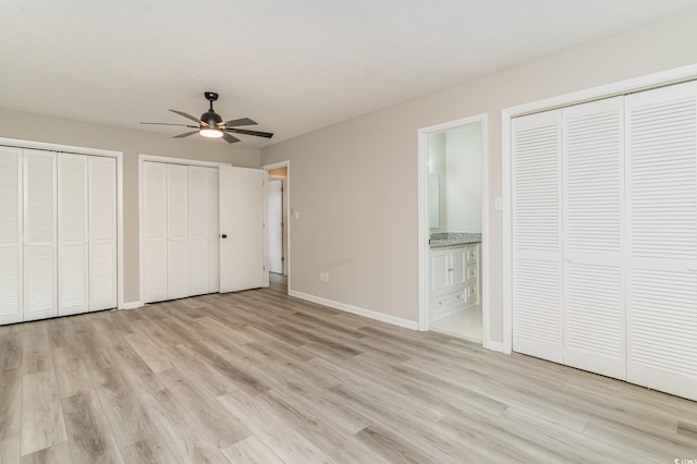 unfurnished bedroom featuring ensuite bath, ceiling fan, a textured ceiling, two closets, and light wood-type flooring