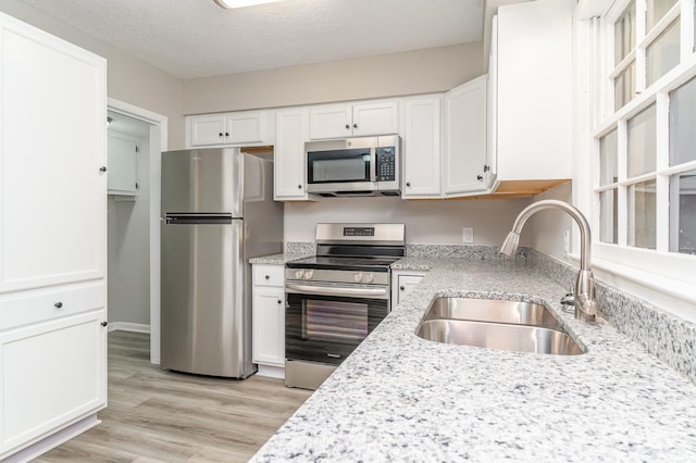 kitchen with sink, light wood-type flooring, a textured ceiling, white cabinetry, and stainless steel appliances