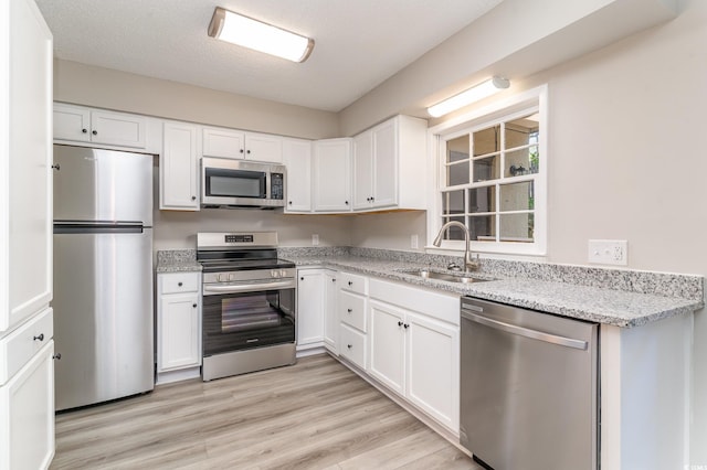 kitchen featuring sink, stainless steel appliances, light hardwood / wood-style flooring, a textured ceiling, and white cabinets