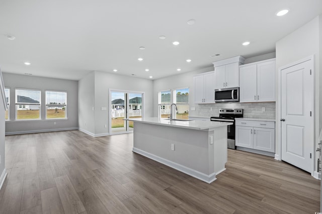 kitchen featuring appliances with stainless steel finishes, light wood-type flooring, backsplash, a kitchen island with sink, and white cabinetry