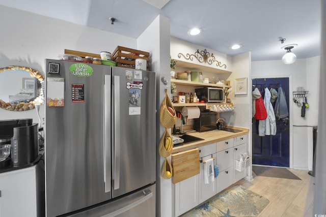 kitchen featuring light wood-type flooring, wooden counters, stainless steel appliances, and white cabinetry