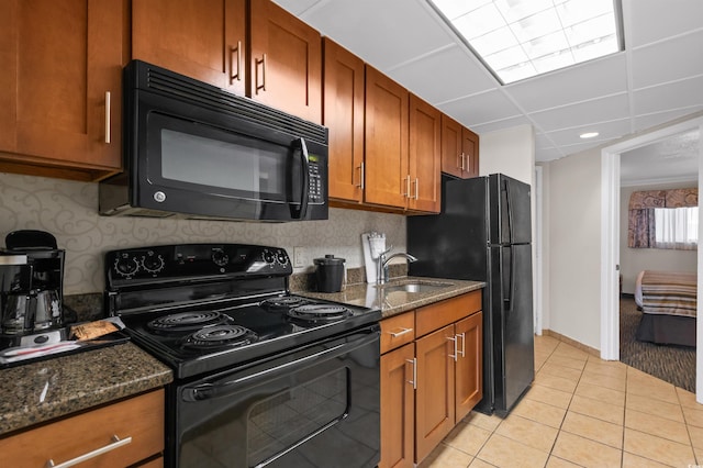 kitchen featuring light tile patterned flooring, a sink, dark stone counters, black appliances, and brown cabinetry