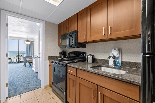 kitchen featuring dark stone counters, black appliances, a water view, sink, and light colored carpet