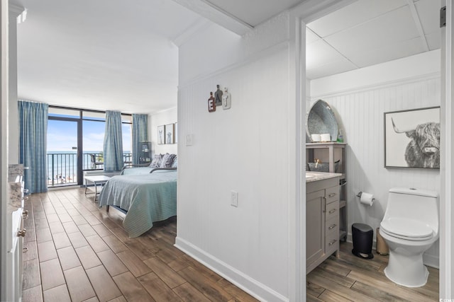 bedroom with access to exterior, expansive windows, baseboards, and wood finished floors